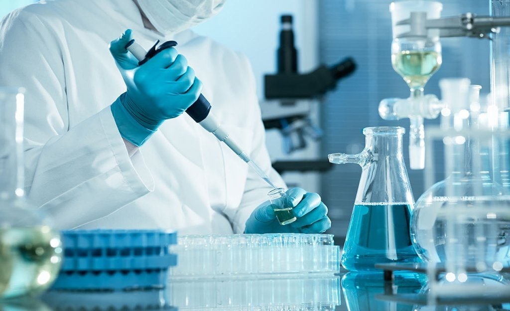 Scientist conducting laboratory tests with pipette and glassware in pharma lab.